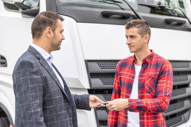 Two men are standing in front of a truck talking to each other.