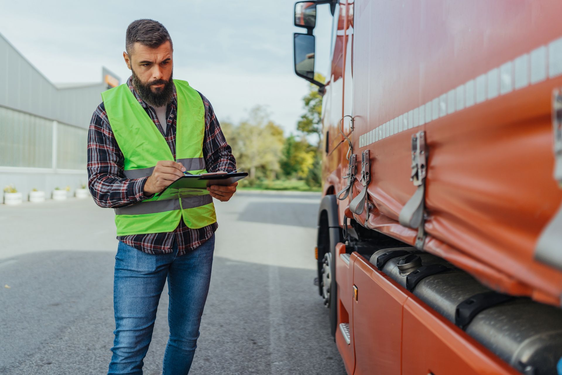 A man in a green vest is standing next to a truck and writing on a clipboard.