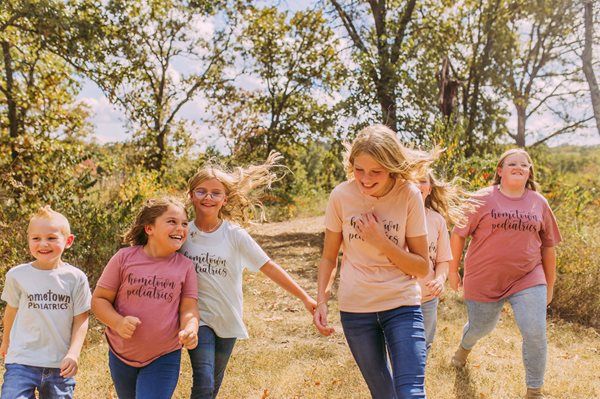 Children walking hand in hand through a sunny grassy field, smiling and laughing