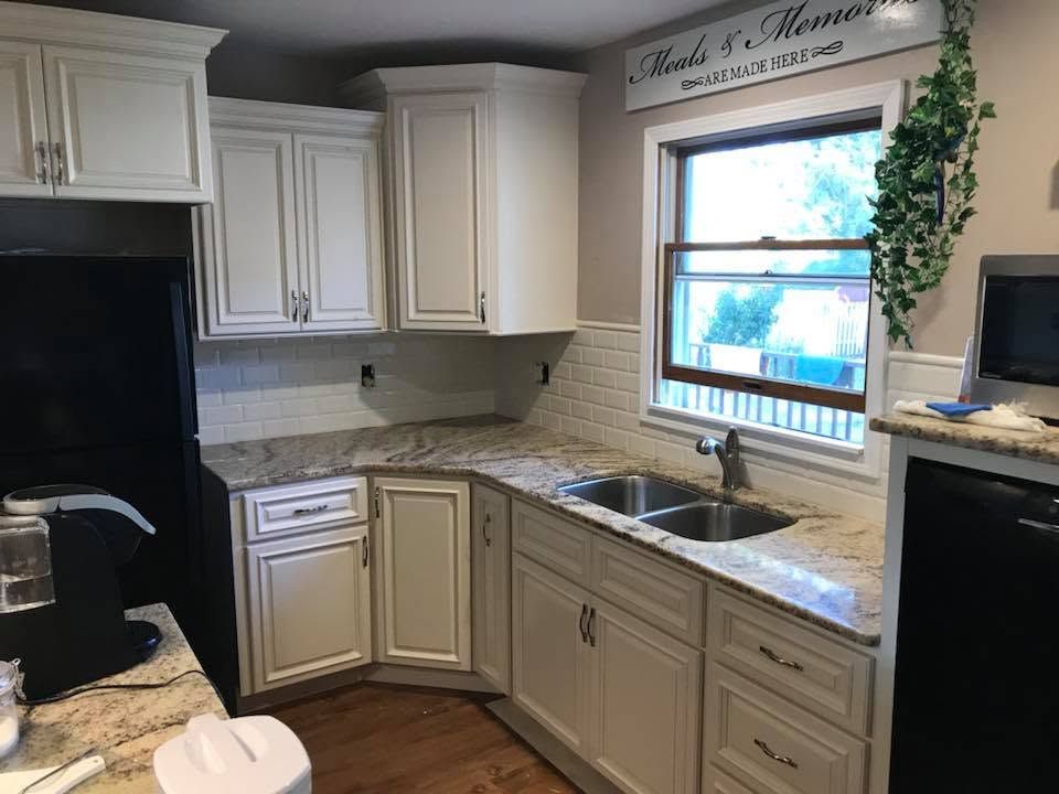Modern L-shaped kitchen with light wood cabinets, white countertops, sink, and built-in oven.