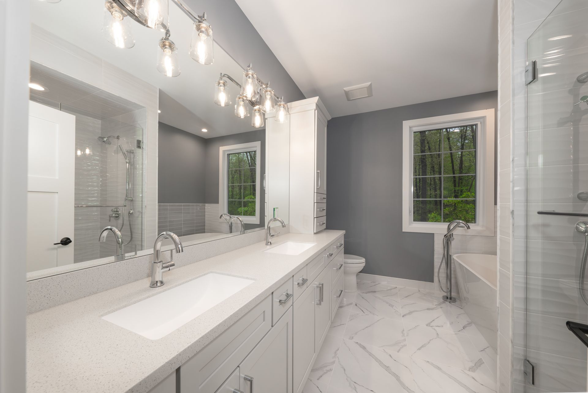 Modern white bathroom with double vanity, large mirrors, glass shower, and gray accent wall