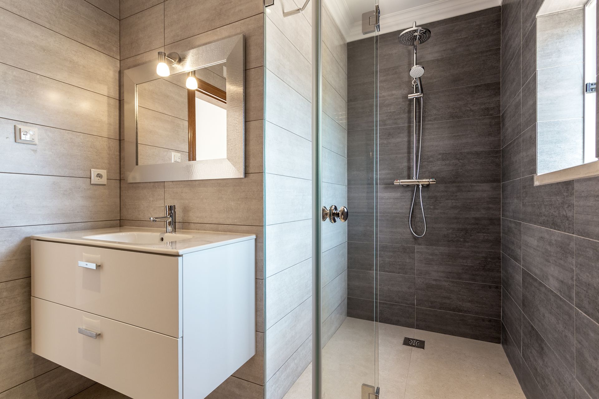 Modern bathroom with white vanity, mirror, and glass shower with gray tile walls