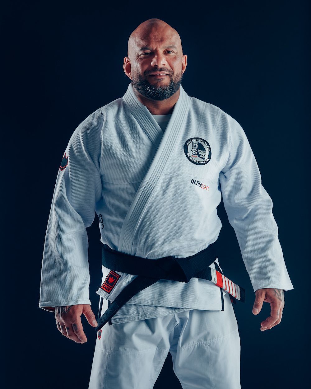 Martial artist in a white gi with black belt standing against a dark background