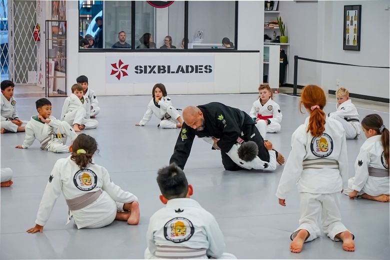 Martial arts class with children in white uniforms practicing on mats while instructor demonstrates a move
