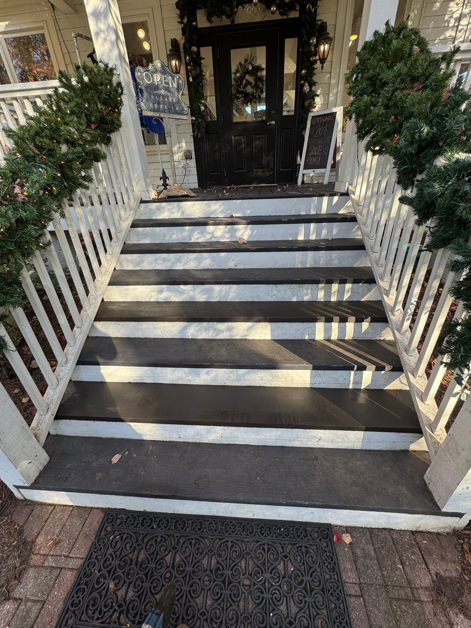 A set of outdoor steps painted with alternating black and white stripes, leading to a dark wooden door with greenery.