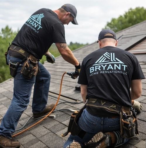 Two roofers in matching black shirts with company branding install shingles on a residential roof.