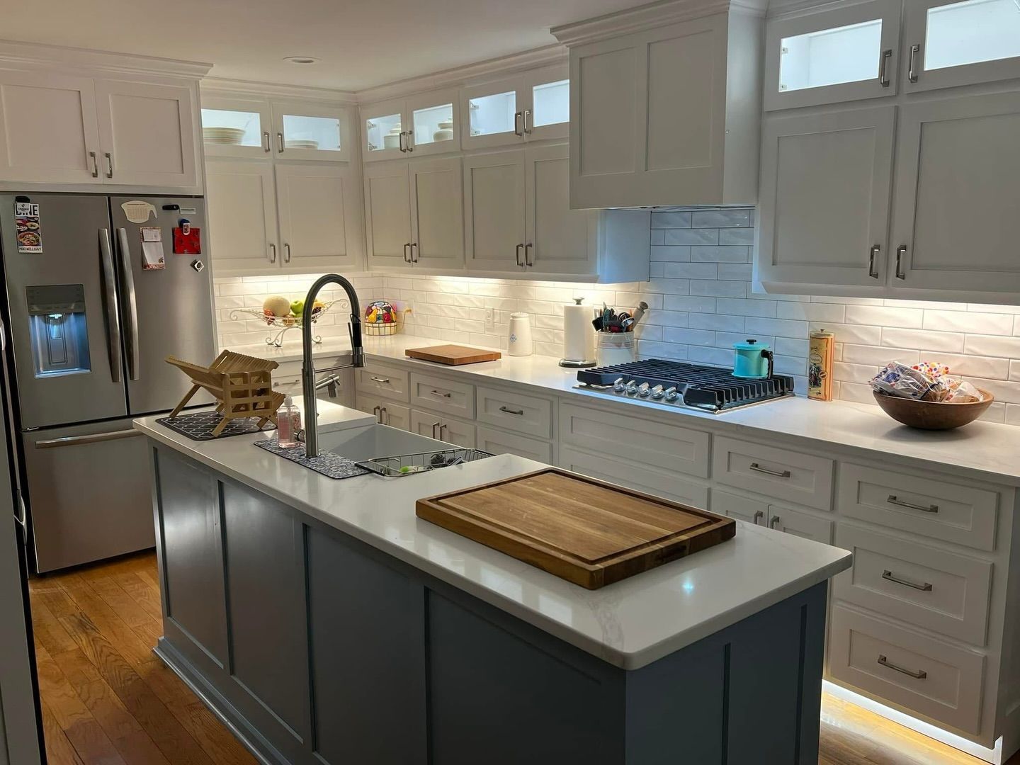 A modern kitchen featuring white cabinets, a navy blue island with a stone countertop, and stainless steel appliances.