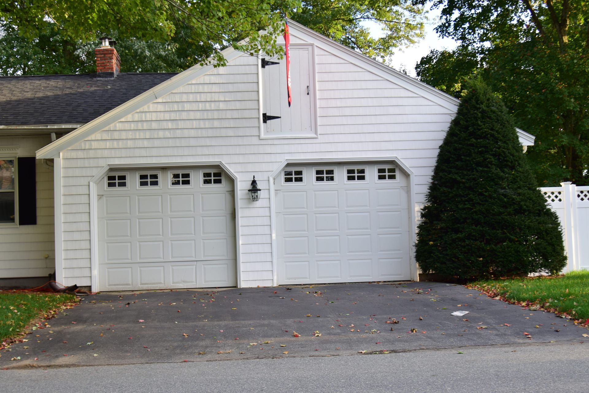 White garage with two doors and a small door above. A tall evergreen bush is to the right.