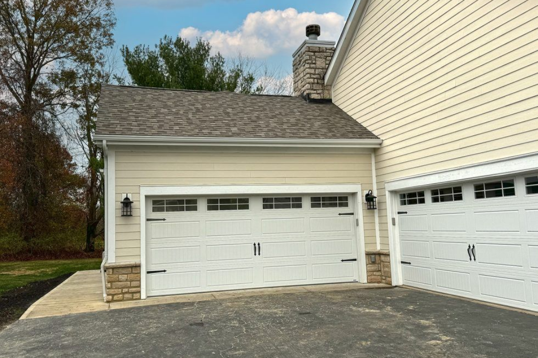 Beige garage with two white doors, chimney, and stone accents under a cloudy sky.