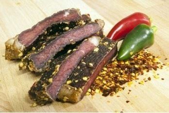 A wooden cutting board topped with slices of meat and peppers.