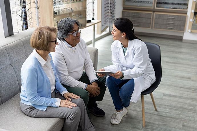 Three people in a clinic waiting area talking with a seated healthcare provider