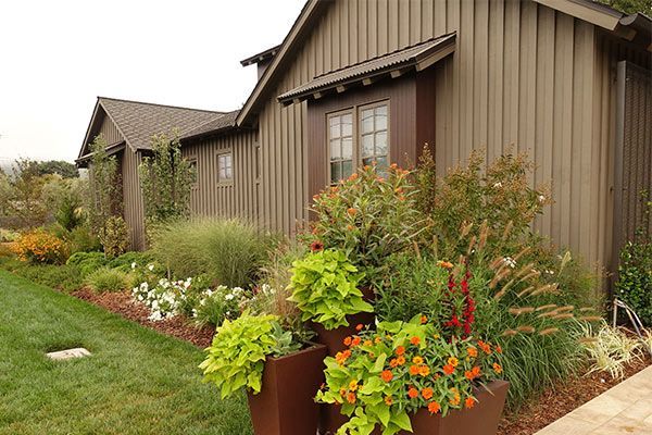 Brown house with a landscaped garden, colorful flowers, and green shrubs along the front yard