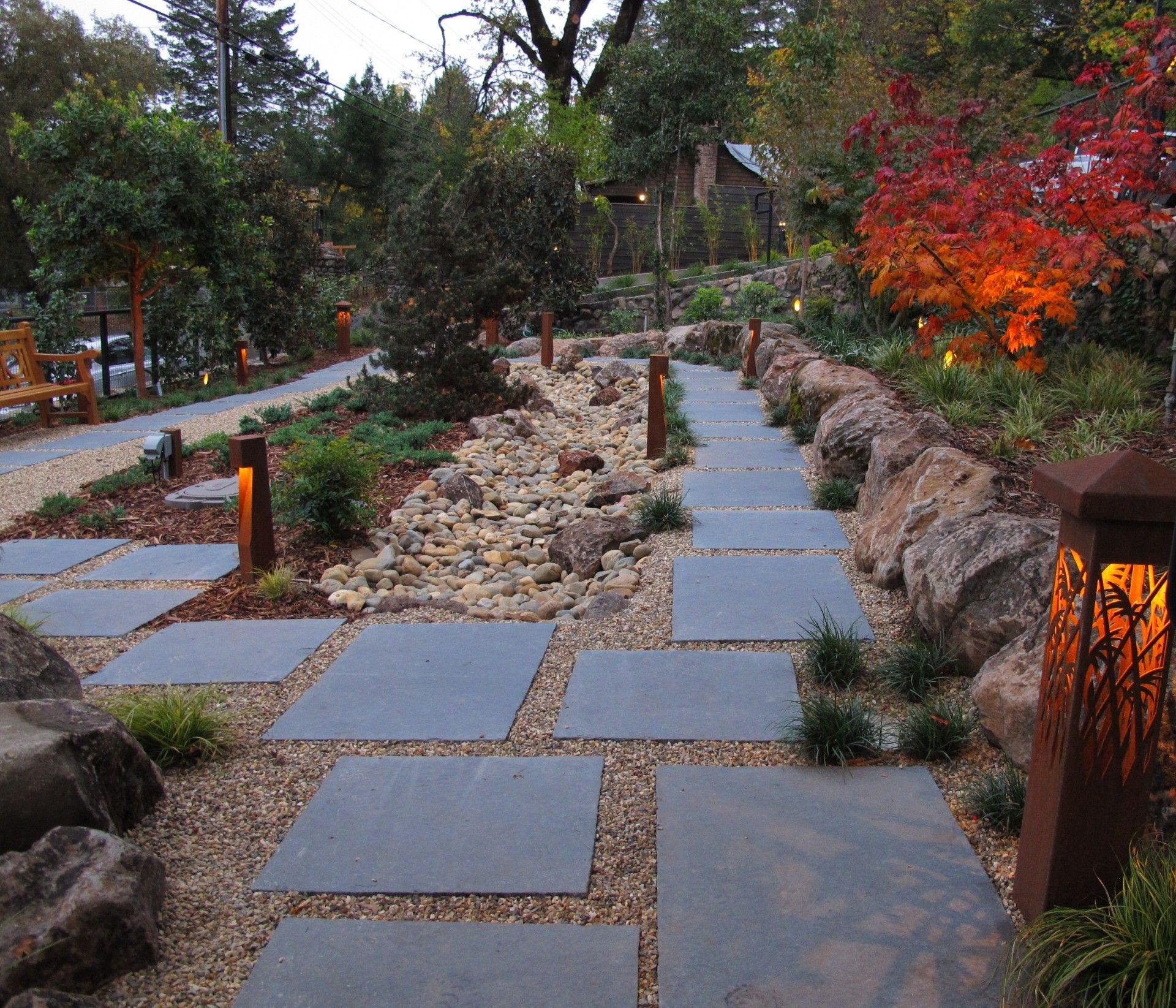 Stone garden path with stepping slabs, lanterns, rocks, and autumn trees at dusk