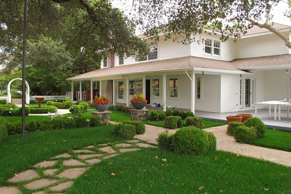 Large white house with a wraparound porch, lush green lawn, and stone garden path.