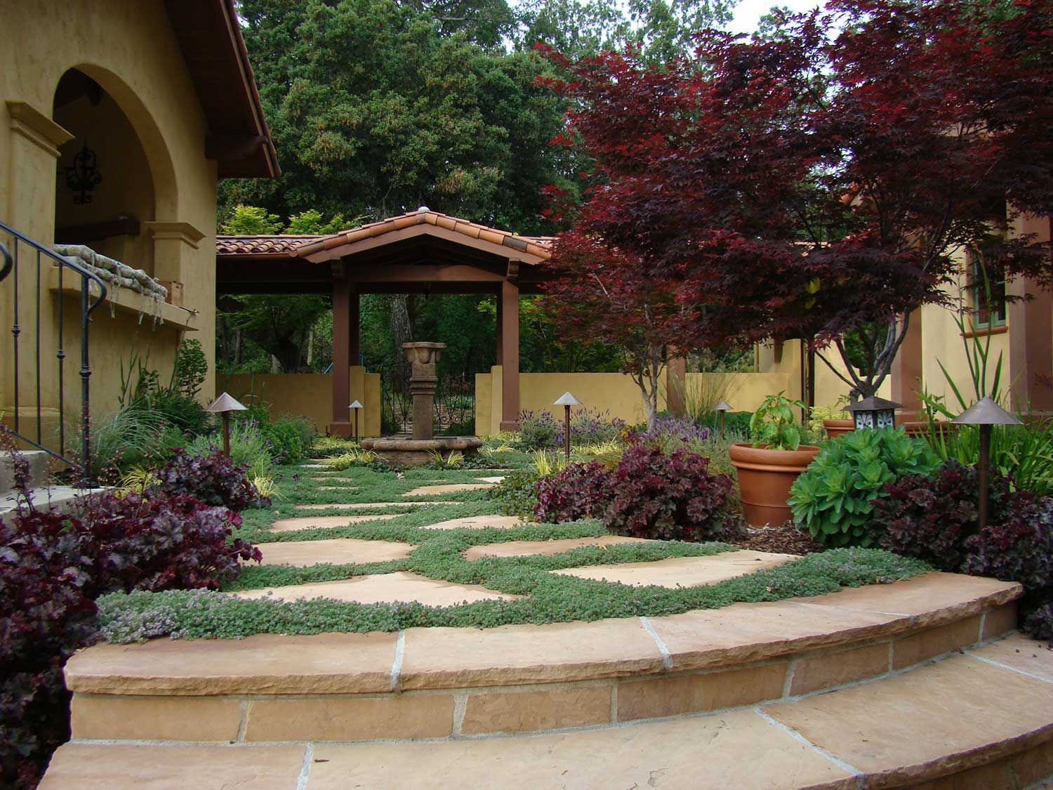 Mediterranean-style courtyard garden with stone steps, pergola, and purple shrubs