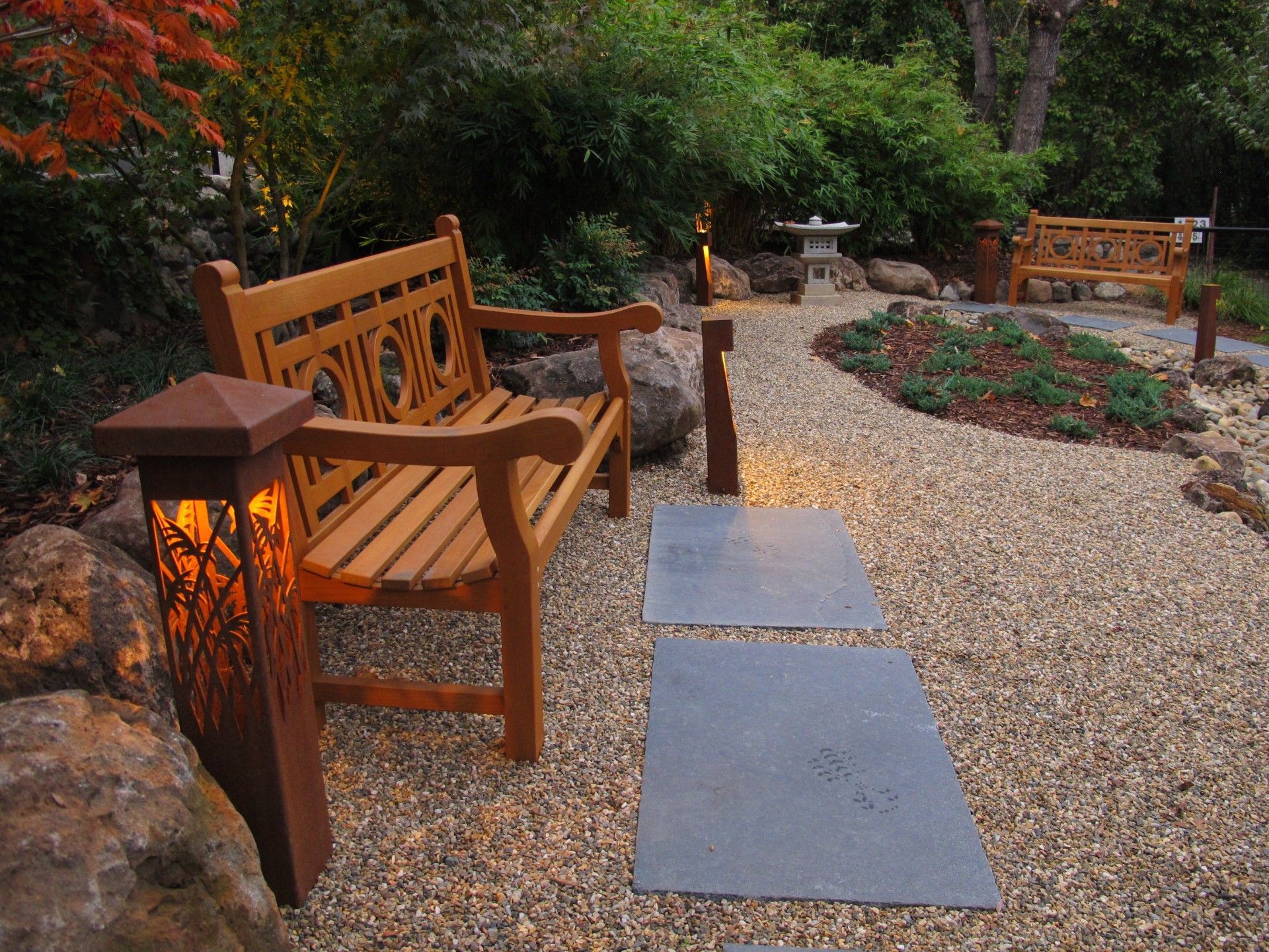 Wooden benches and lanterns line a gravel garden path with stone stepping stones and flowers.