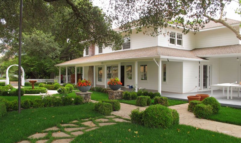 Two-story white house with a covered porch, green lawn, and landscaped garden paths