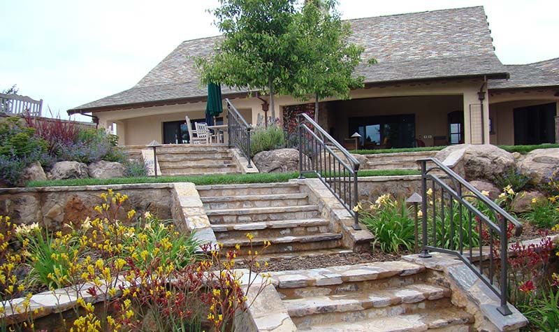 Stepped stone walkway leading to a rustic house with a shingled roof and landscaped garden