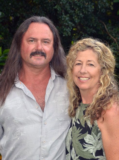 Two smiling adults posing outdoors, with greenery in the background.