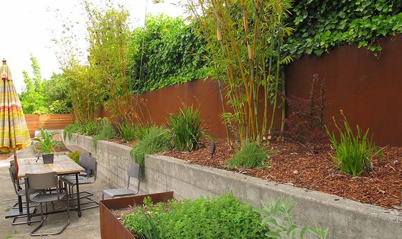 Backyard patio with outdoor seating, raised planters, and a tall brown fence lined with greenery