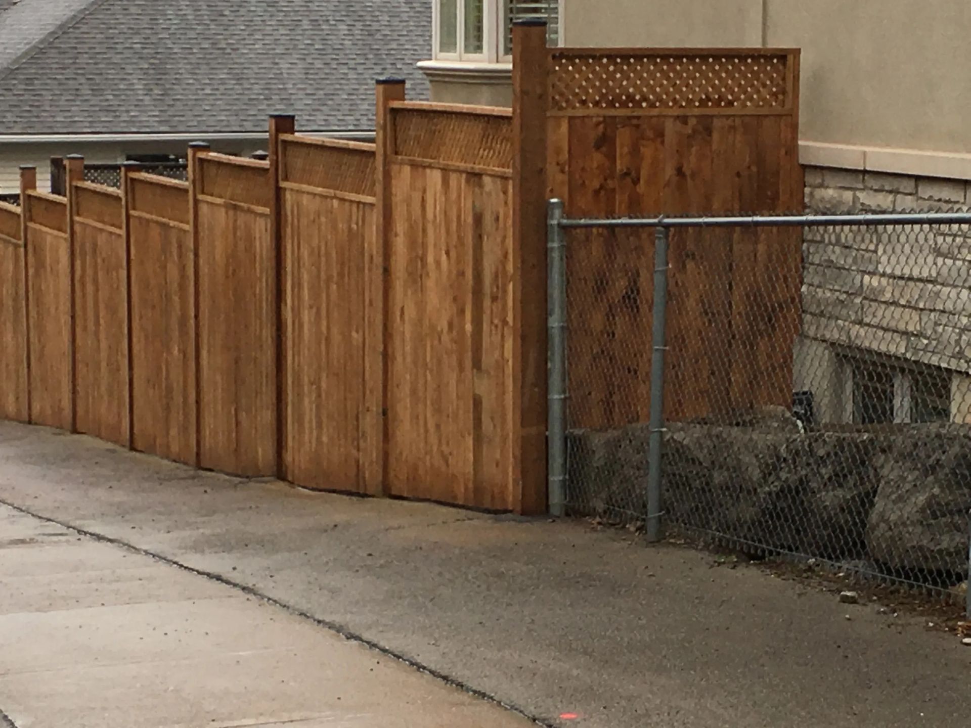 A wooden fence along a sidewalk next to a chain link fence