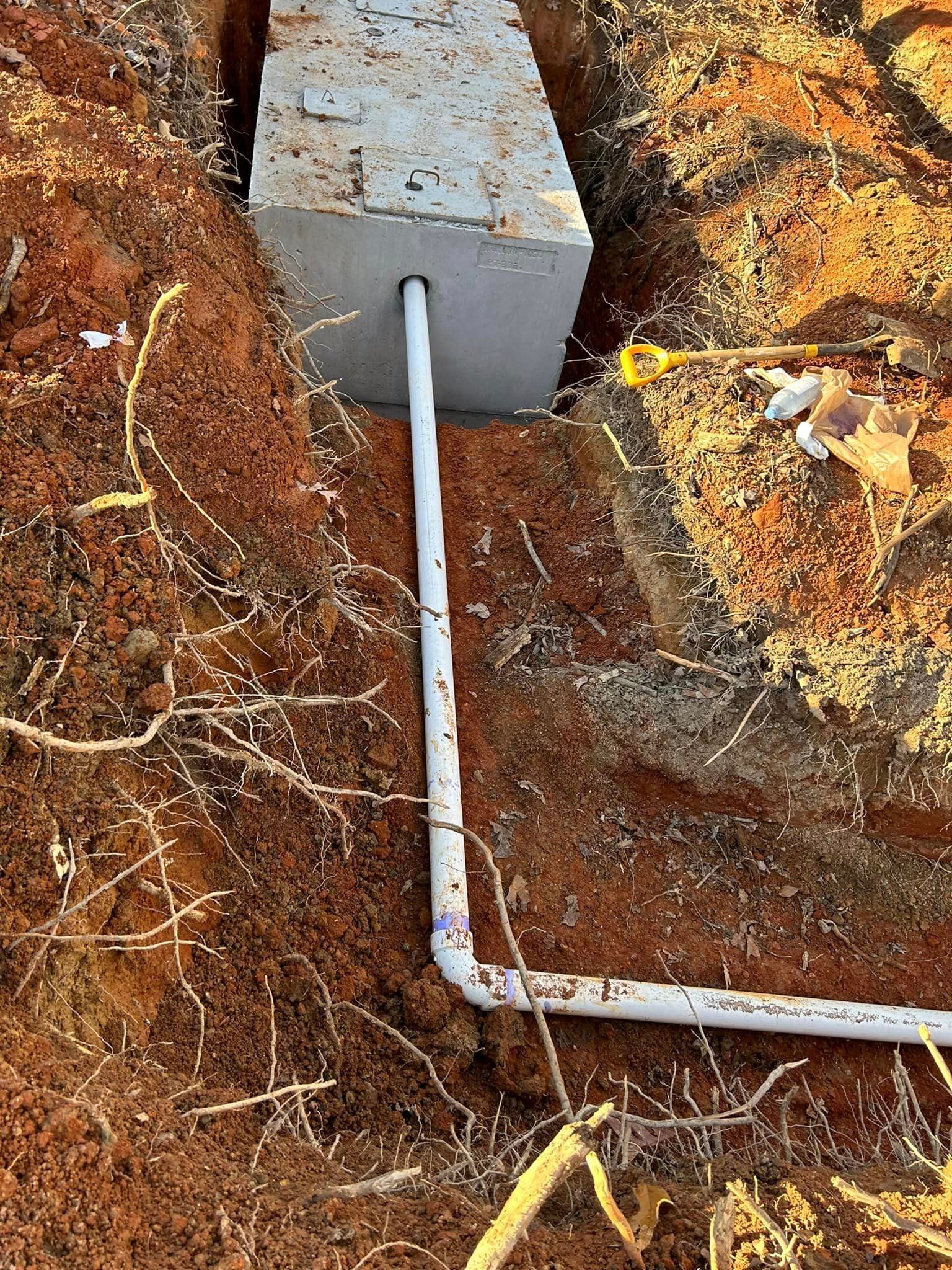 A white pipe is connected to a concrete block in the dirt.