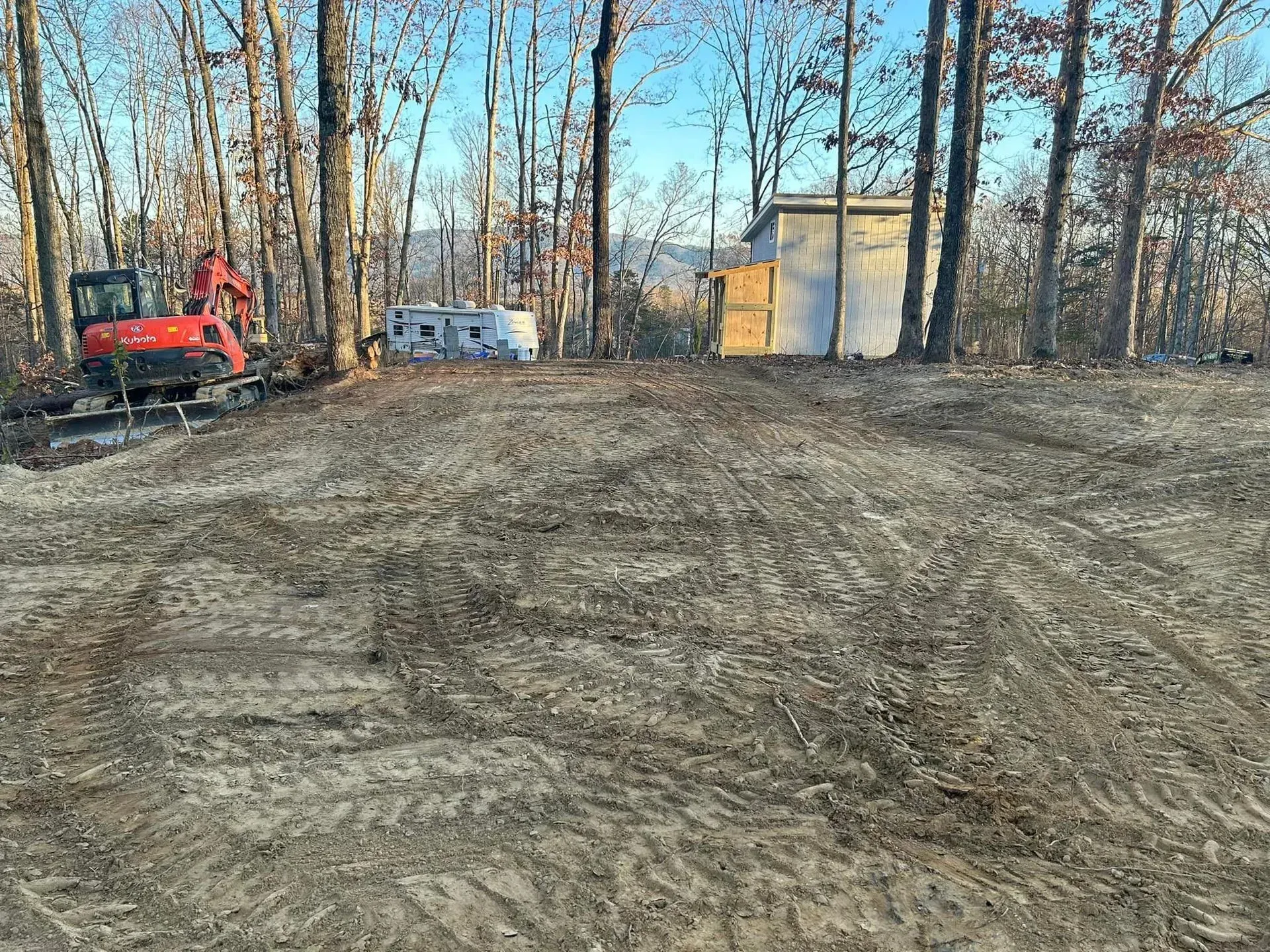 A red excavator is sitting in the middle of a dirt field.