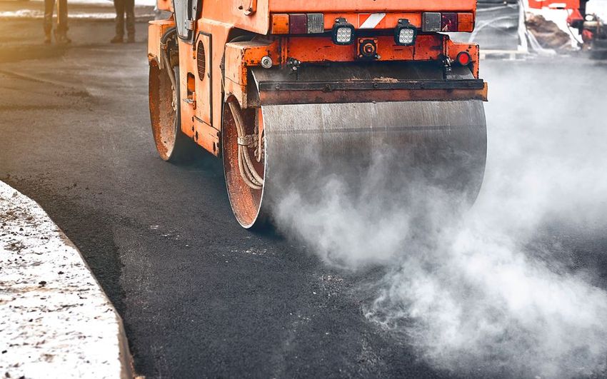 Orange road roller paving a wet street, with steam rising from the asphalt.