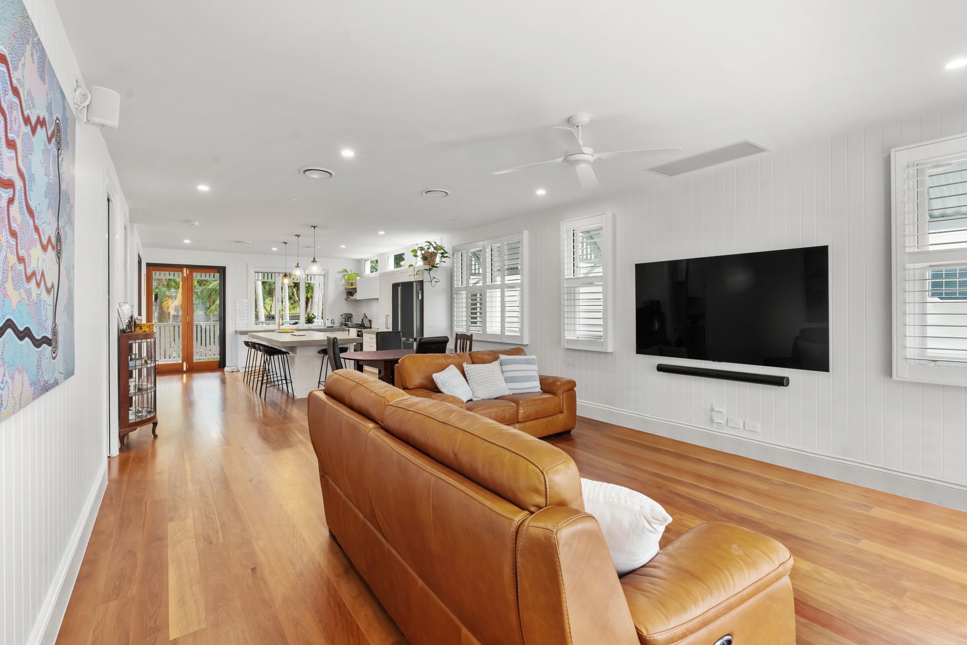 Bright modern living room with tan sofa, hardwood floors, and wall-mounted TV