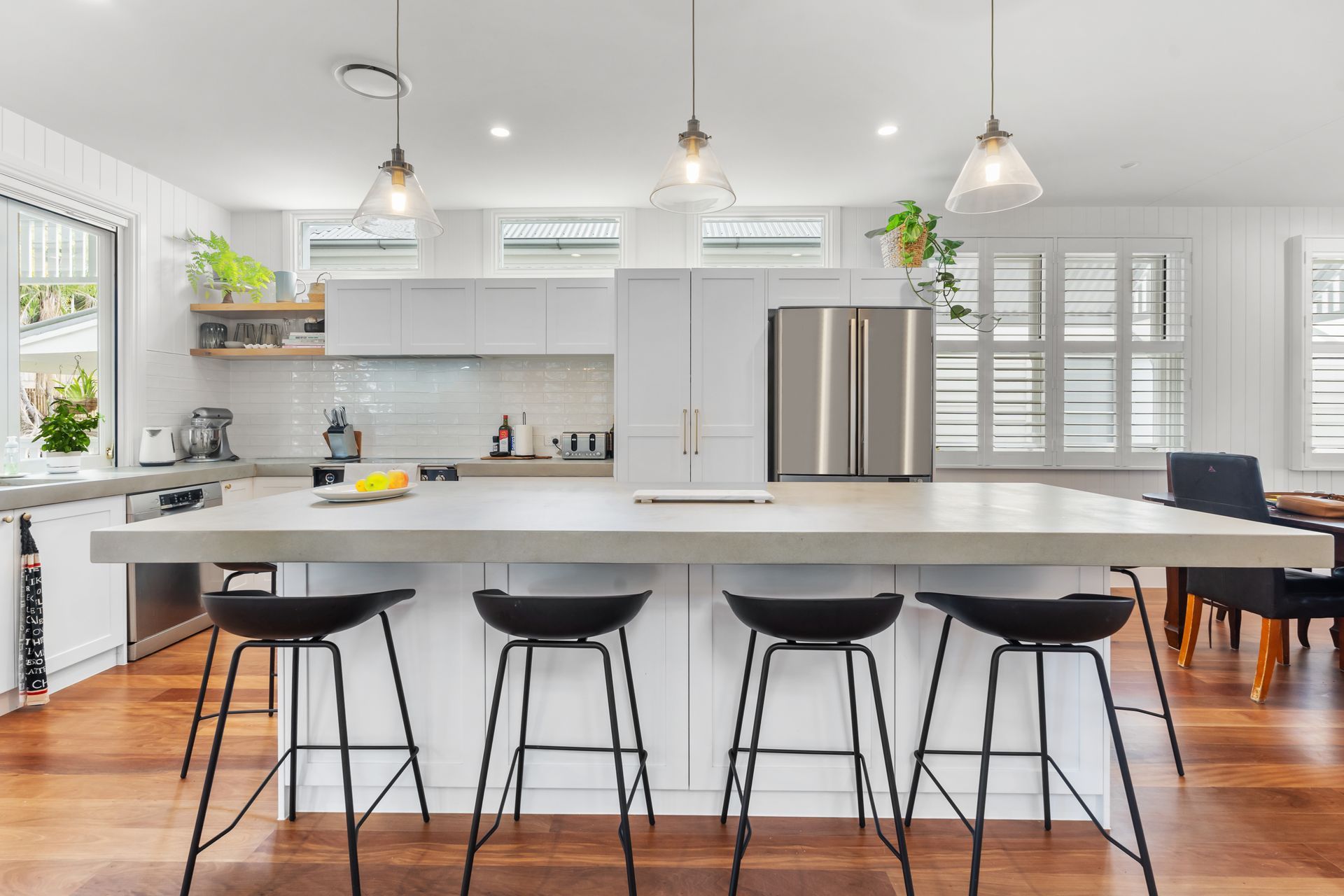 Bright modern kitchen with white cabinets, stainless appliances, and a long island with four black stools.
