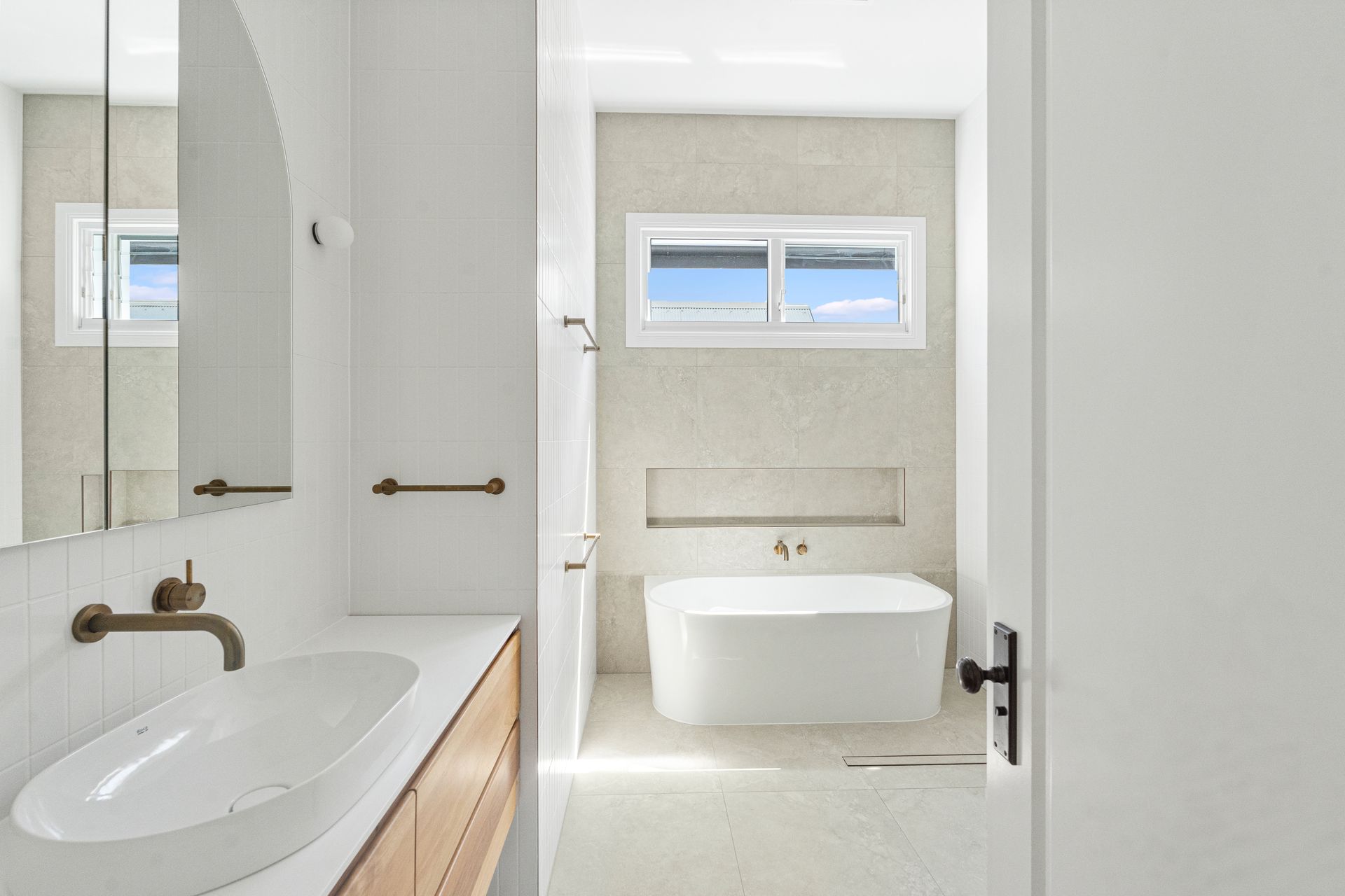 Bright white bathroom with a sink, bathtub, mirror, and small window.
