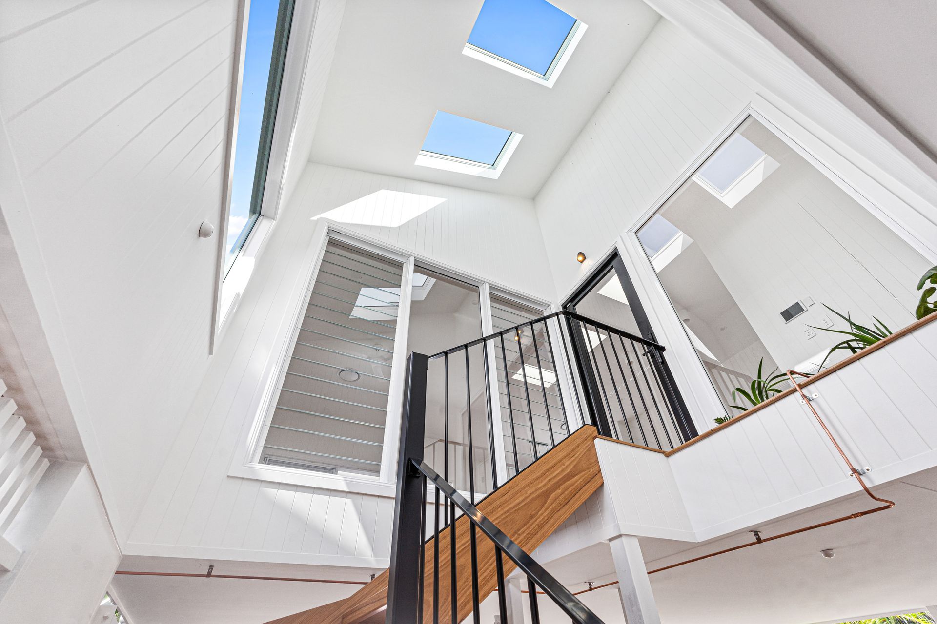 Bright modern stairwell with skylights, white walls, and black railing in a spacious atrium