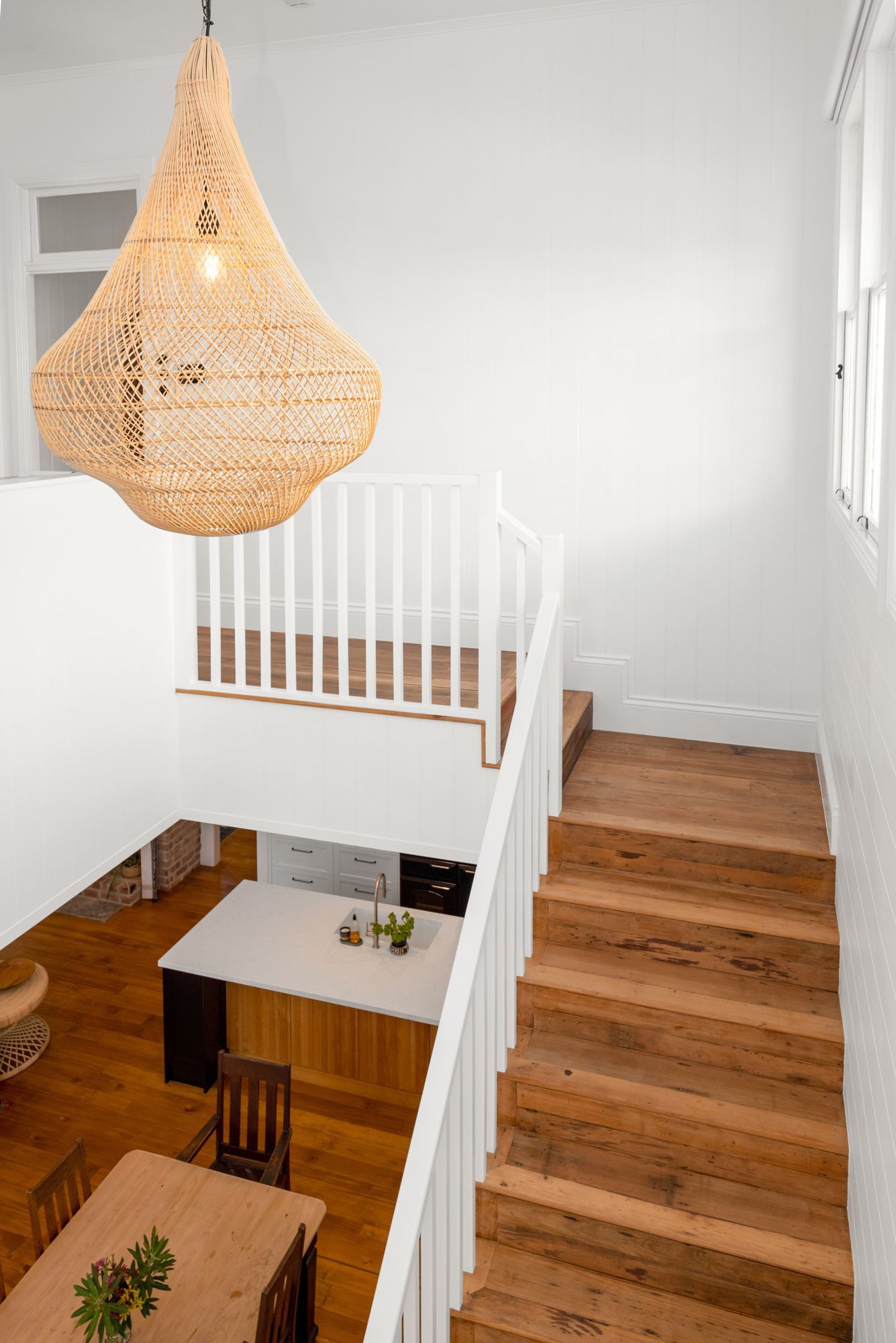 Bright stairwell with wooden stairs, white railing, and a woven pendant lamp over an open interior space