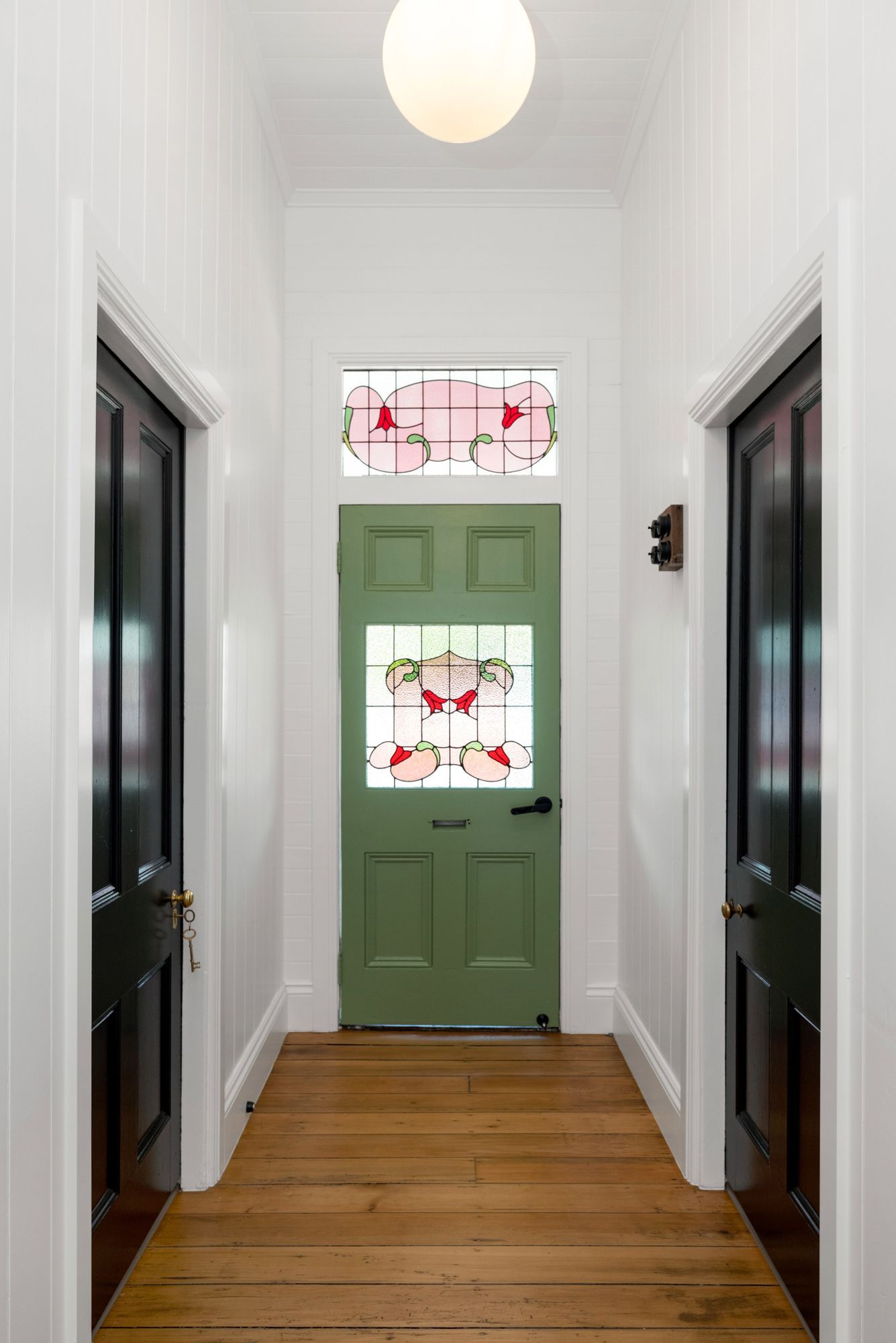 Narrow hallway with white walls, hardwood floor, and a green front door with floral stained glass panels.