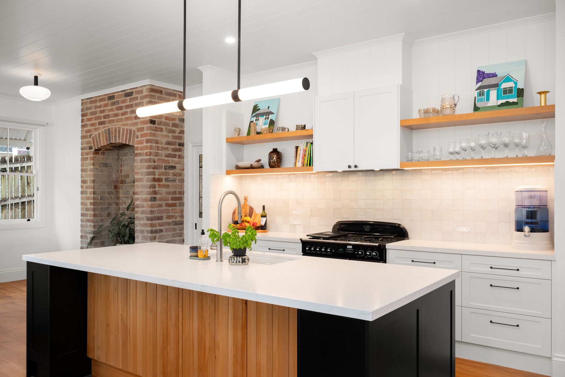 Modern white kitchen with island, brick accent wall, pendant lights, and open shelving