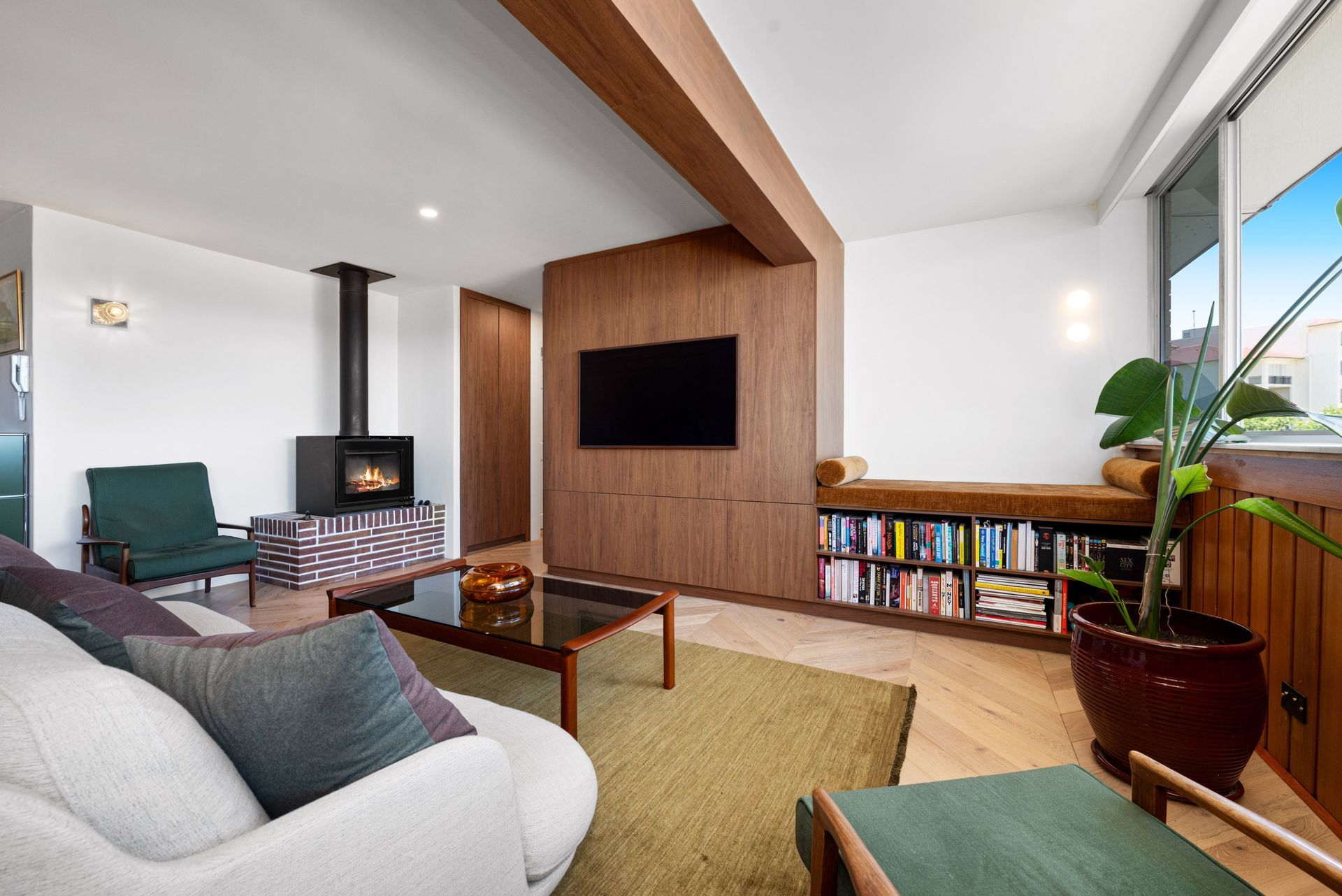 Modern living room with a wall-mounted TV, wood accent wall, green chairs, and large windows