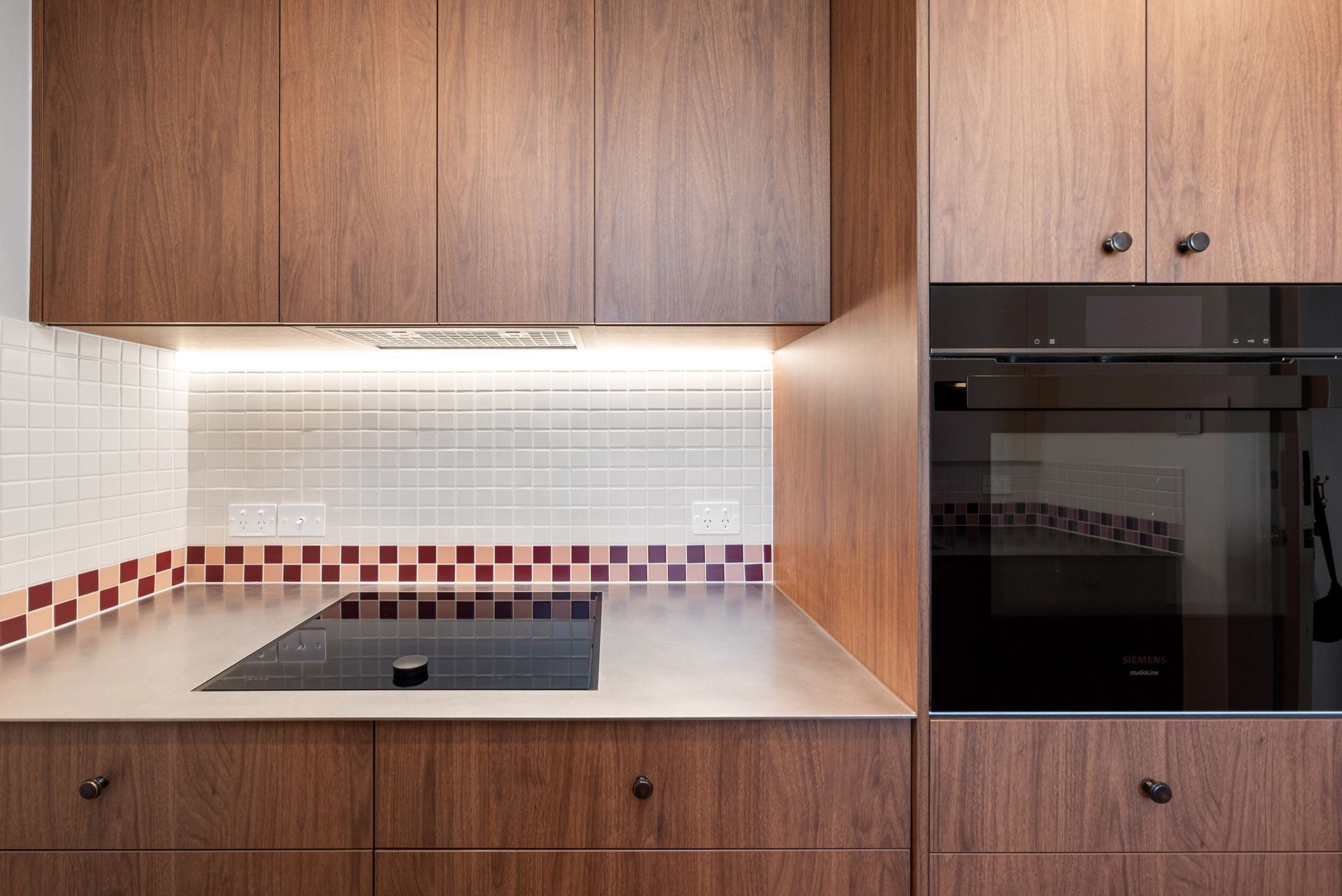 Modern kitchen with wood cabinets, white tile backsplash, cooktop, and built-in oven.