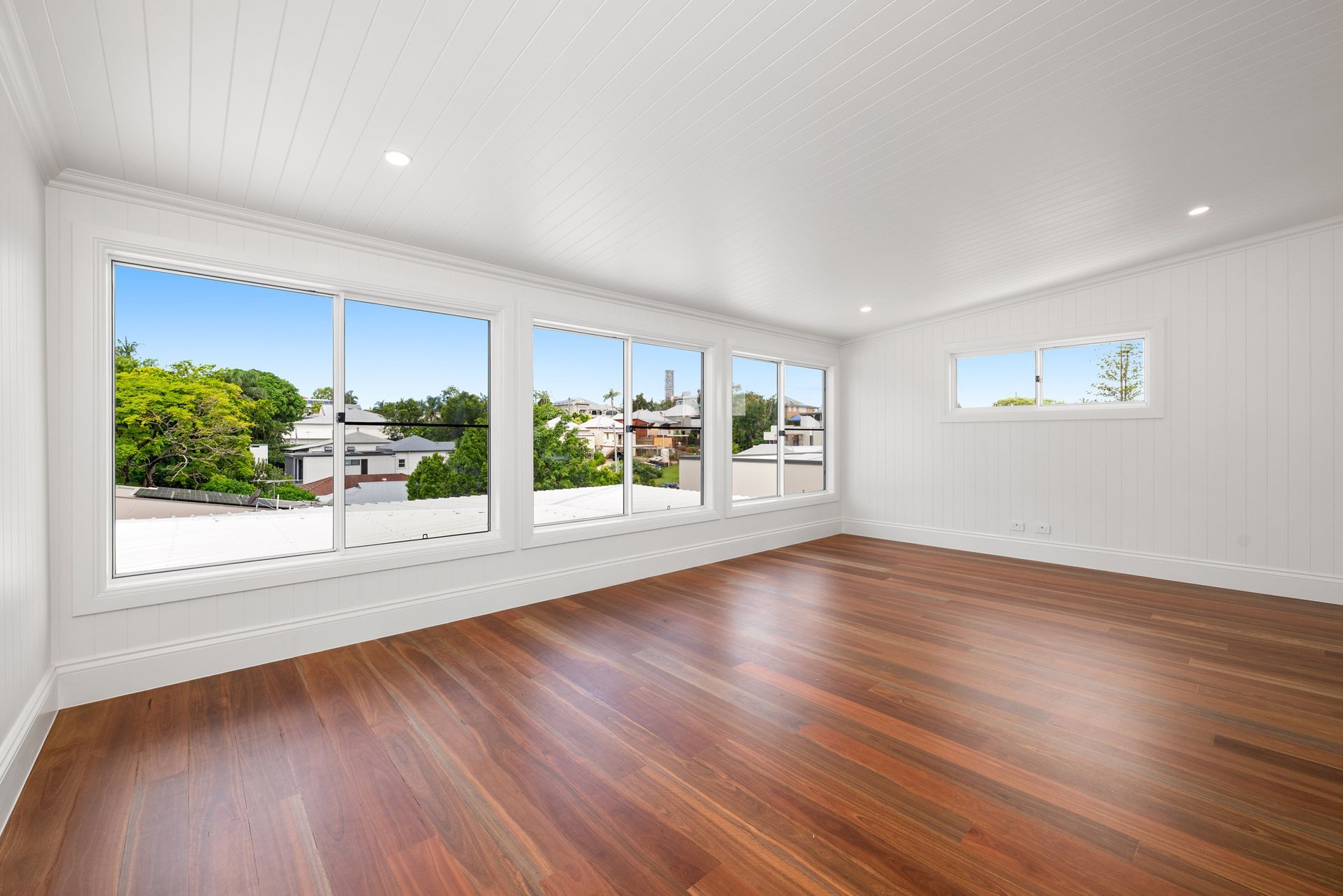 Bright empty living room with hardwood floors and large windows overlooking greenery