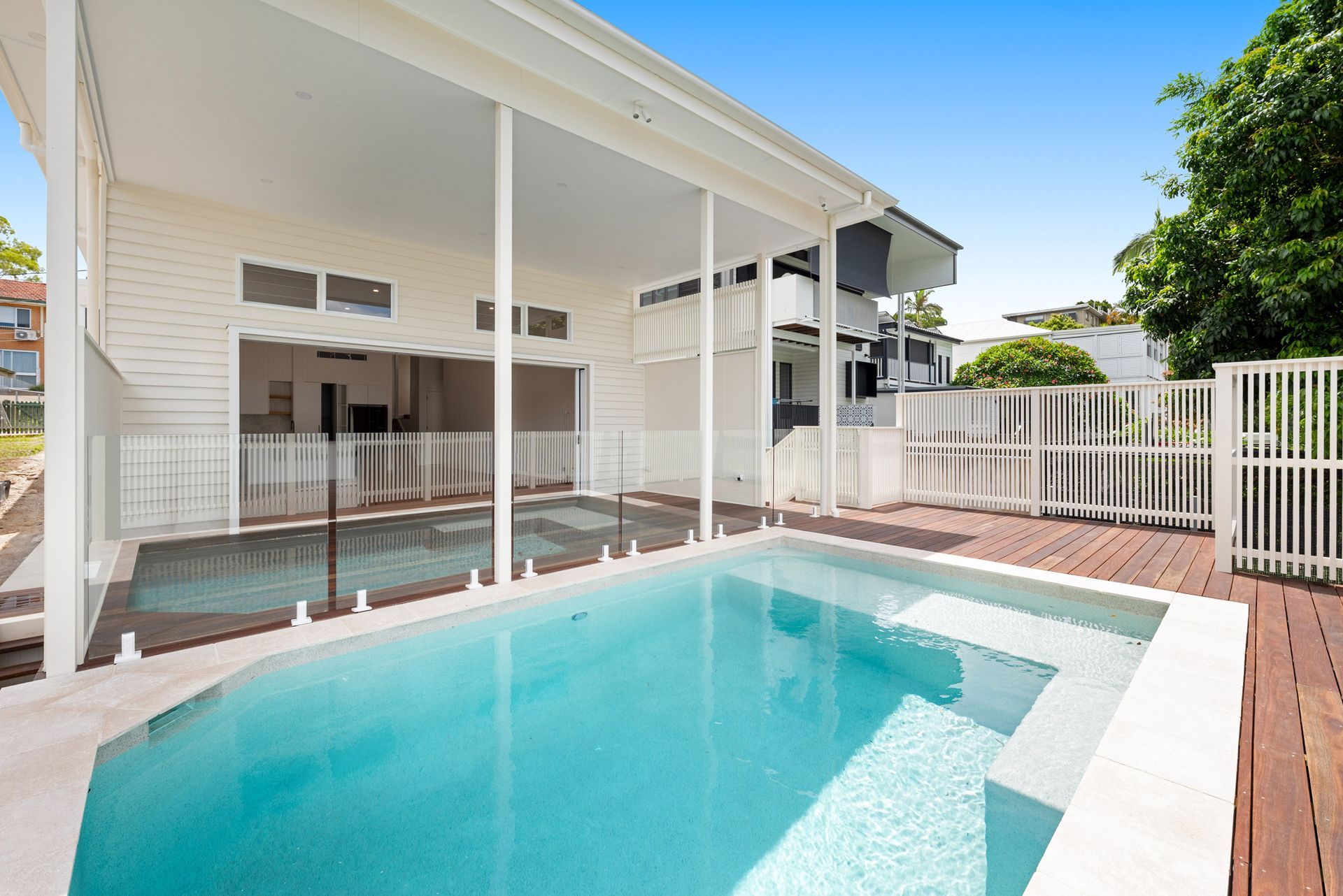Backyard pool with turquoise water beside a covered patio and white fence on a sunny day