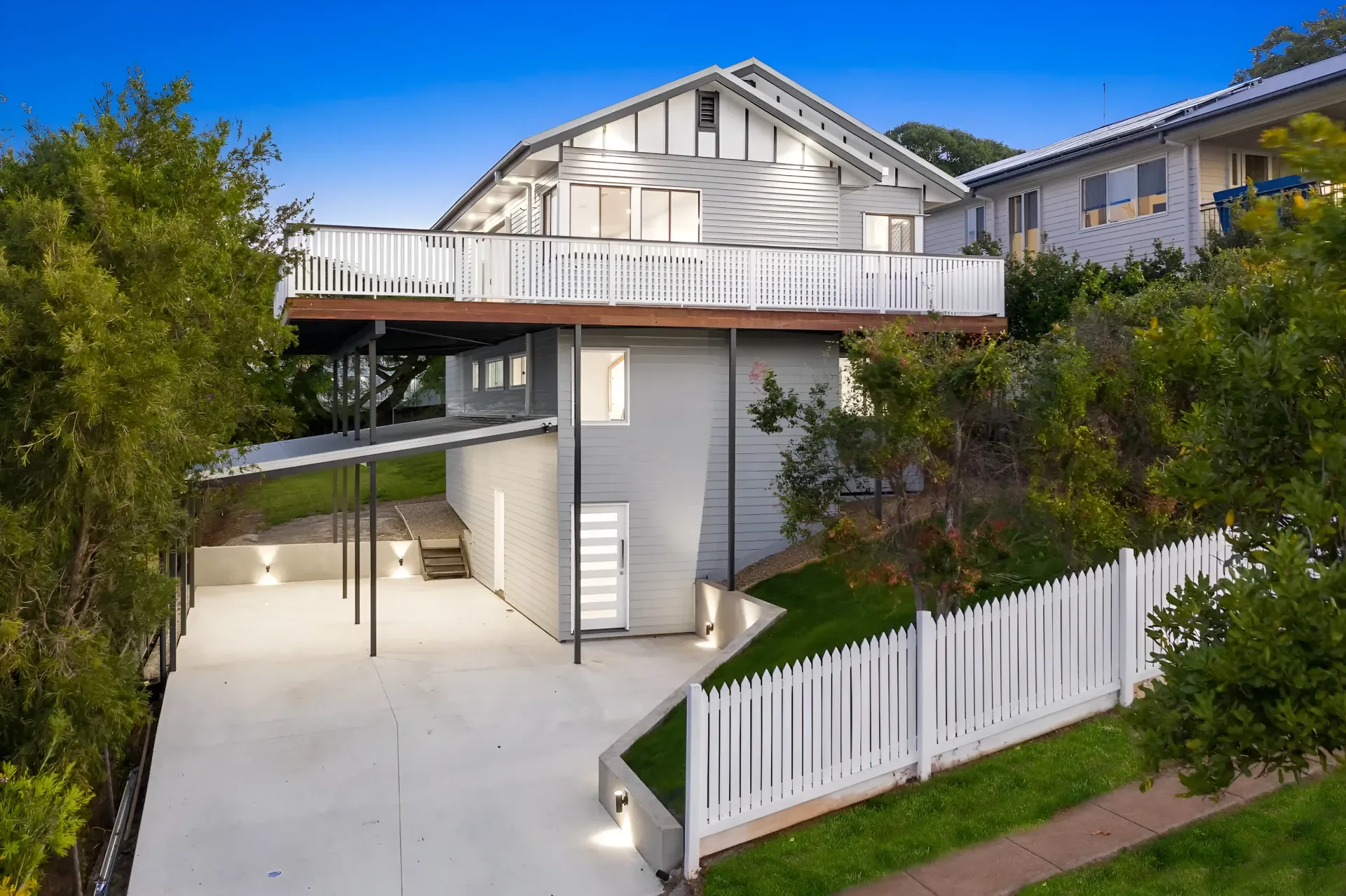 White two-story house with balcony, ornate railings, and garage behind a paved driveway
