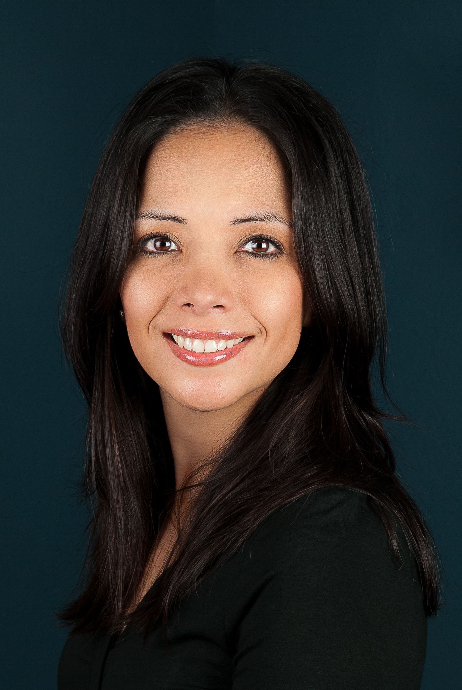 A woman wearing a blue jacket and pearls is smiling for the camera.