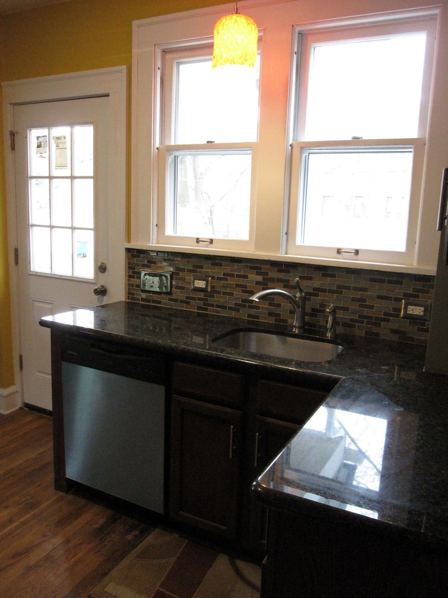 Kitchen with dark cabinets, granite countertops, and stainless steel dishwasher. Windows above sink with mosaic backsplash.