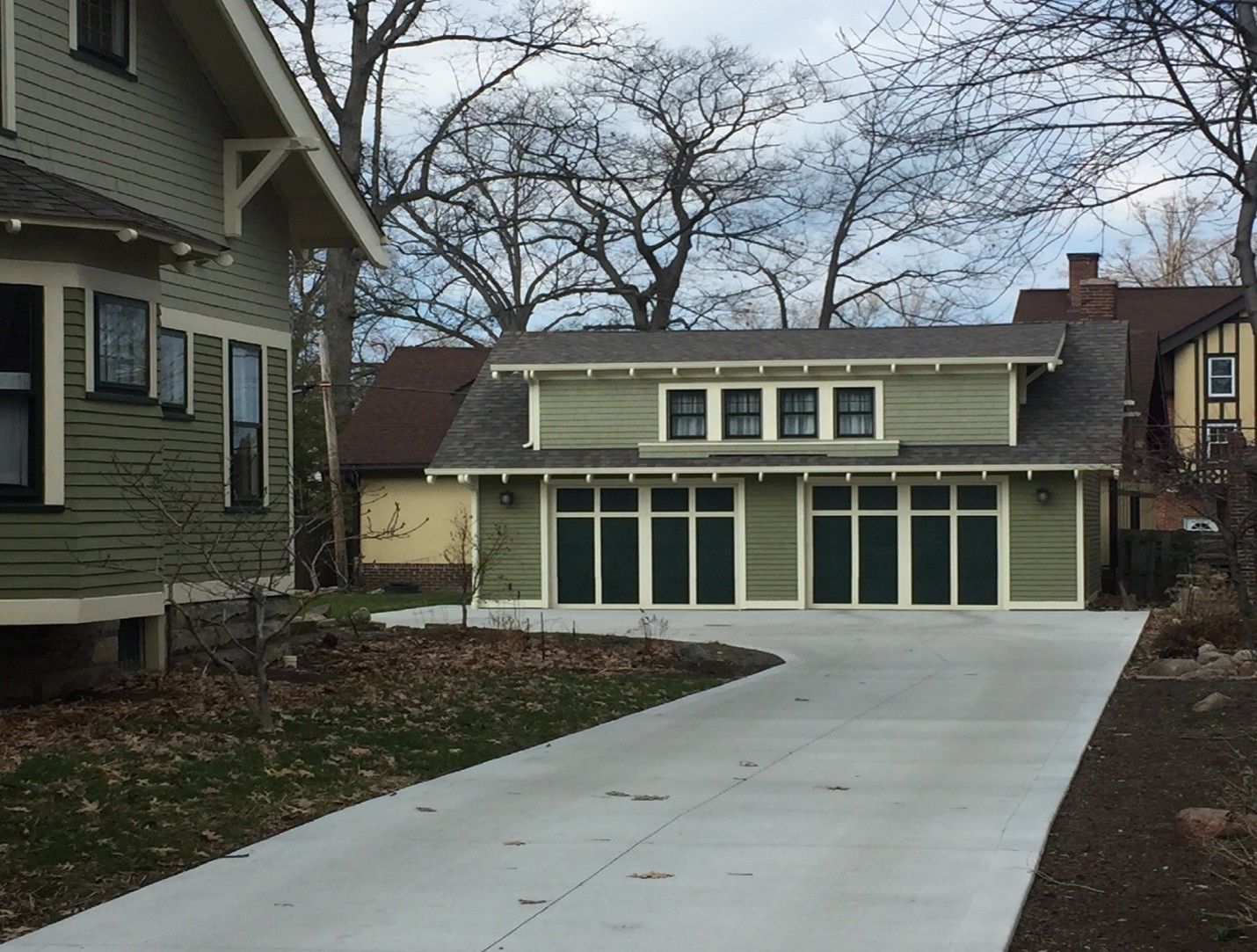 Two-car green garage with matching trim, concrete driveway, and adjacent houses on a cloudy day.