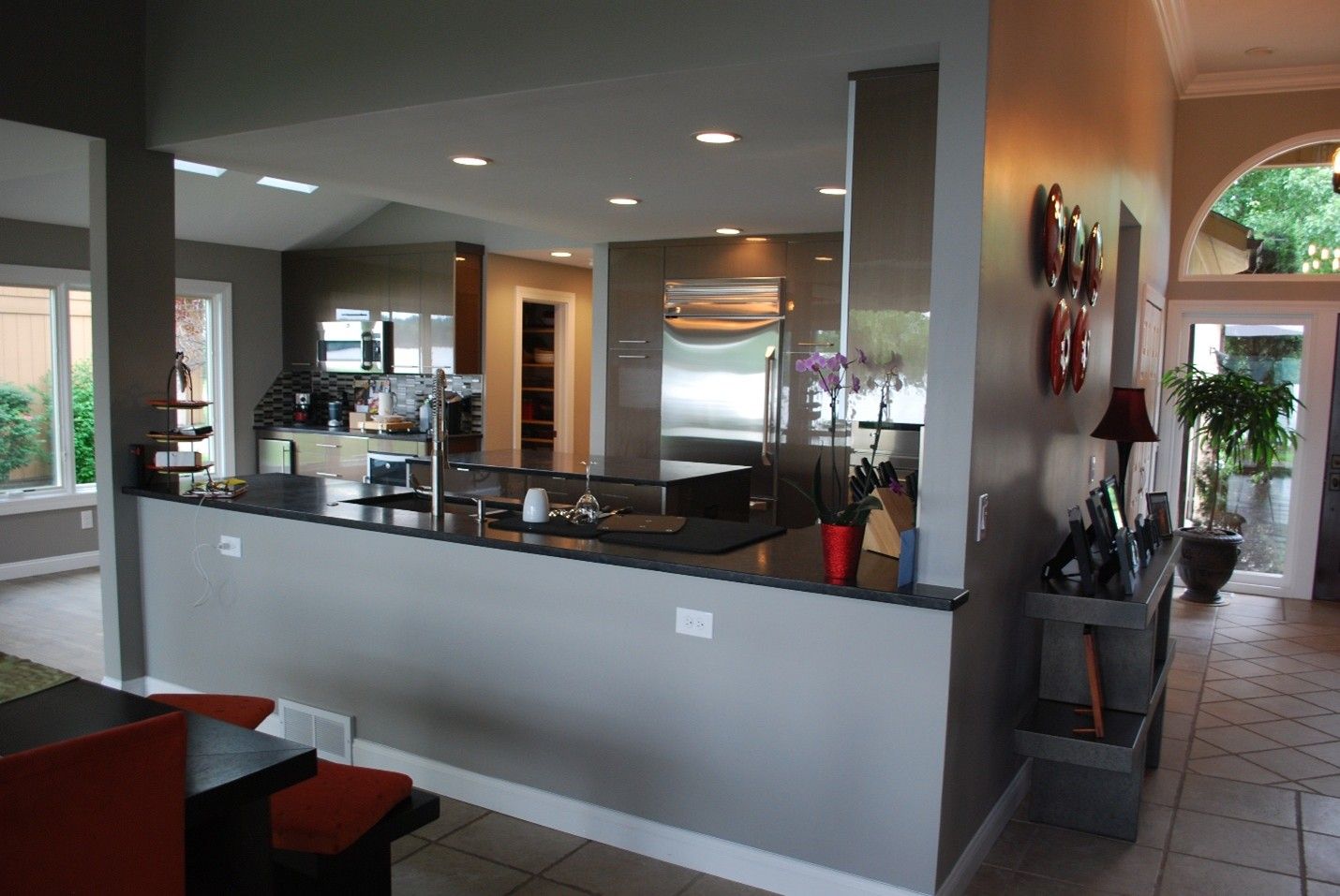 Kitchen with a dark countertop and stainless steel appliances; dining area with orange chairs.