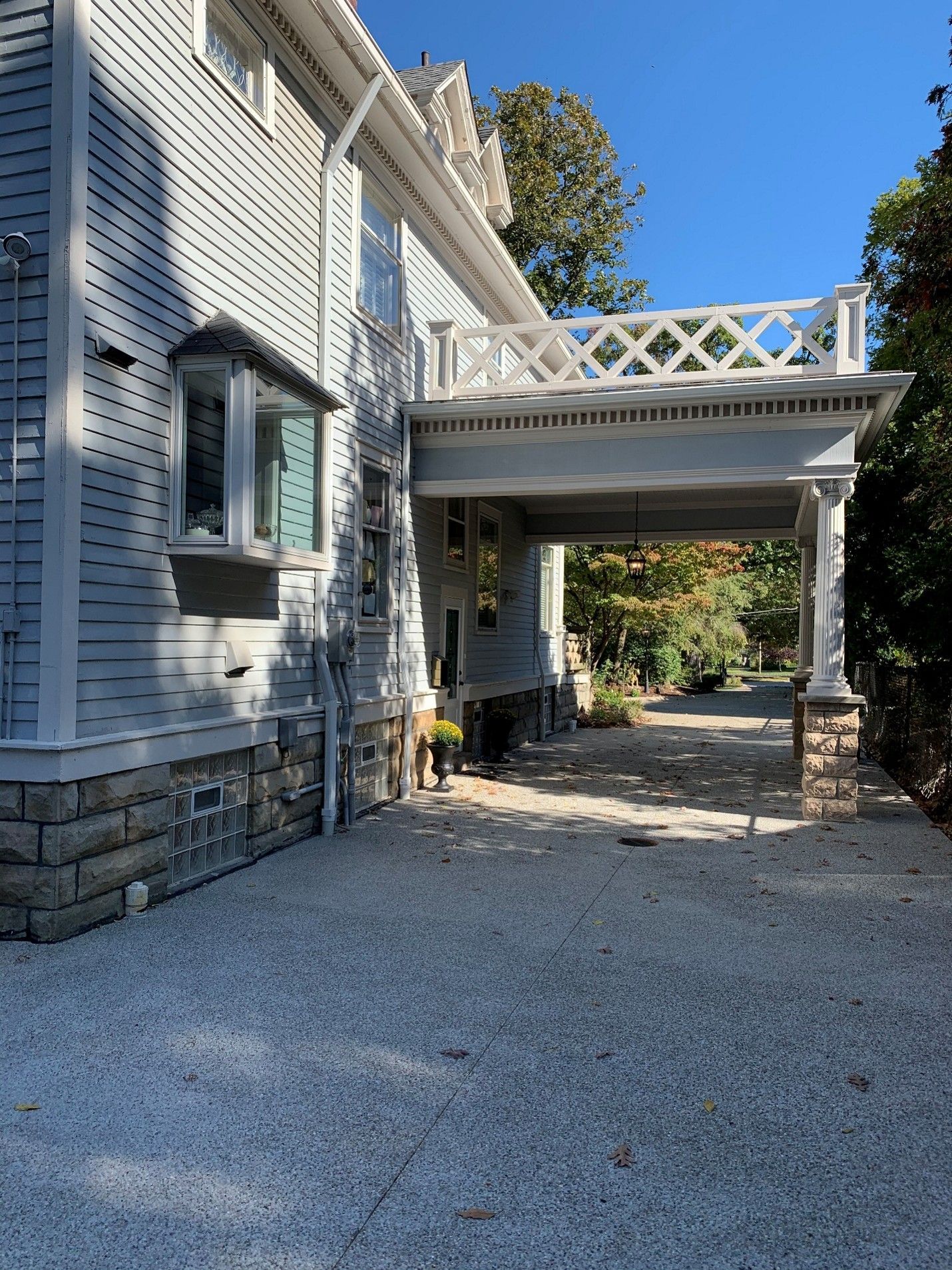 Light blue house with stone foundation, a gravel driveway, and a covered porch with a balcony.