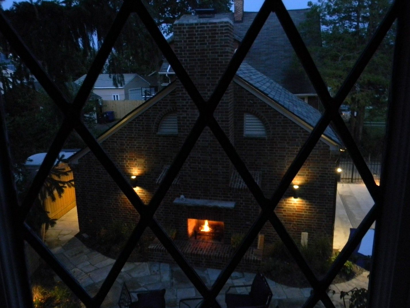 Brick building with fireplace viewed through diamond-patterned window at dusk; lights illuminate the exterior.