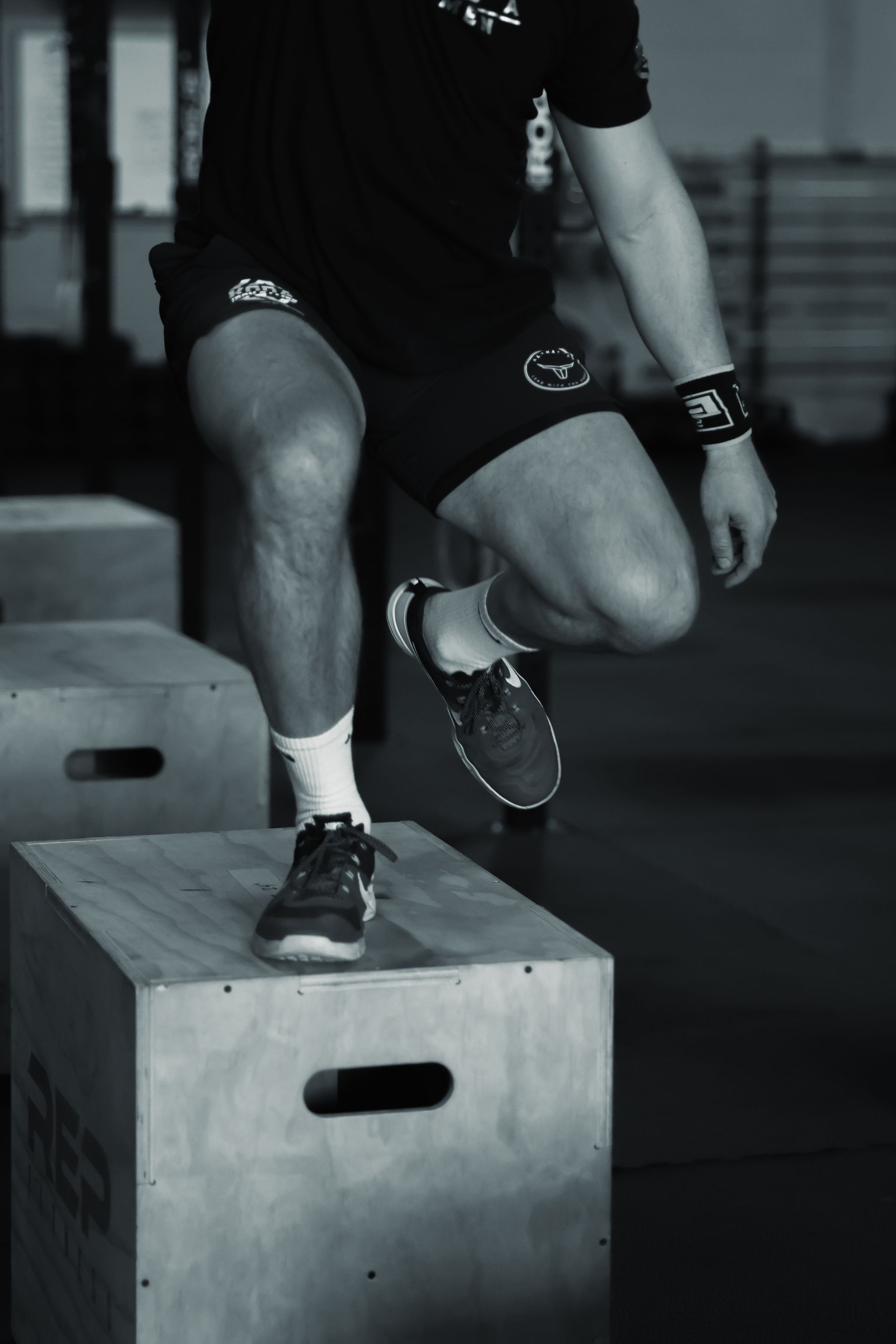 Athlete stepping onto a wooden plyometric box in a gym in Northglenn, CO, wearing shorts and sneakers.