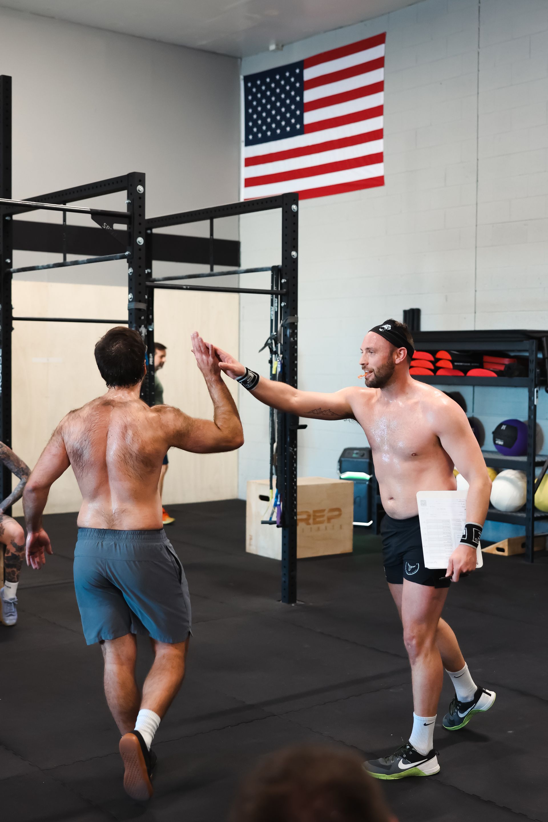 Two men high-five in a gym beneath a large American flag.