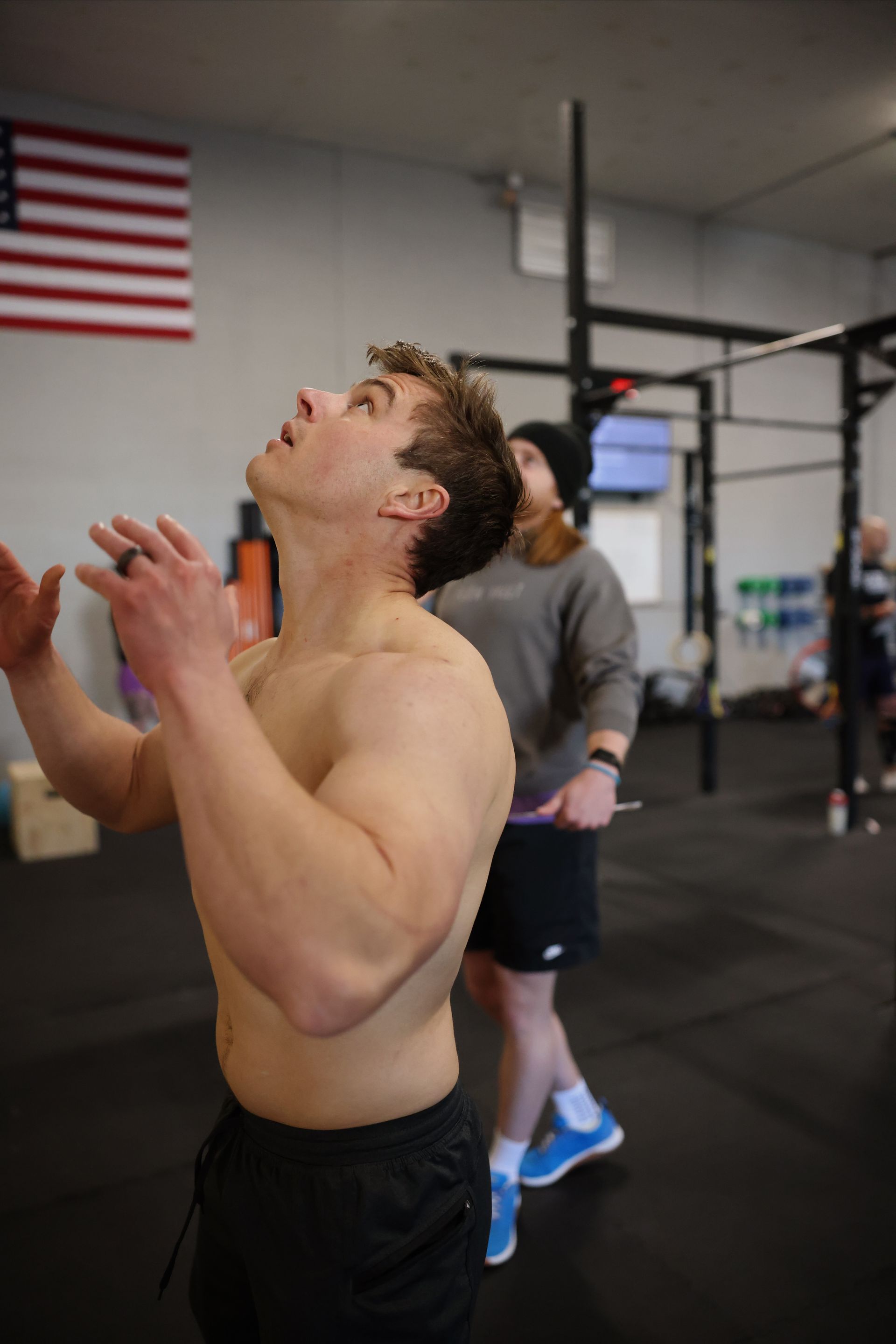 Man in gym in Northglenn, CO reaching upward toward a pull-up bar, with American flag on the wall behind him.
