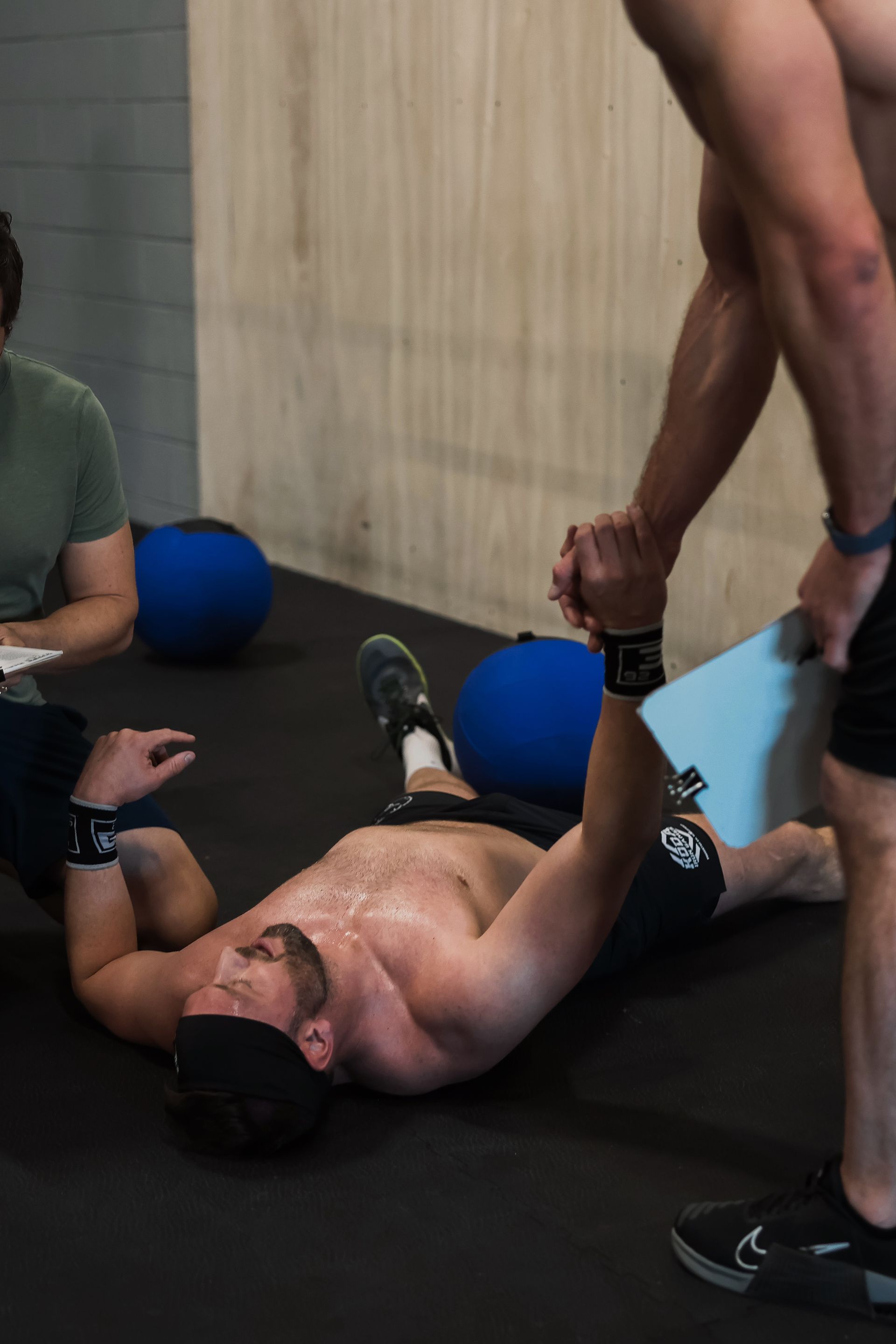 Person lying on gym floor in a gym in Northglenn, CO while another helps stretch their arm beside blue exercise balls